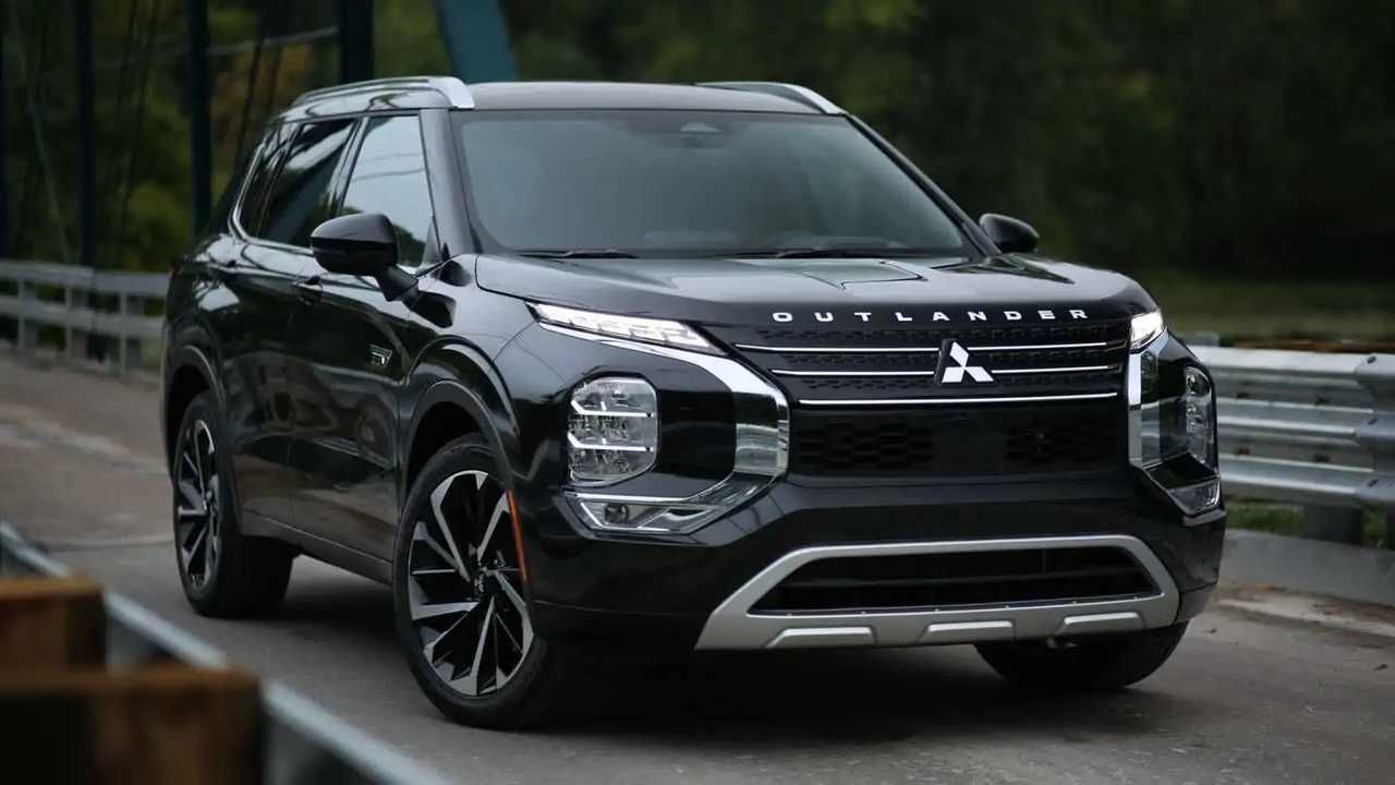 Black Mitsubishi SUV driving on a wet road near a guardrail, front three-quarter view