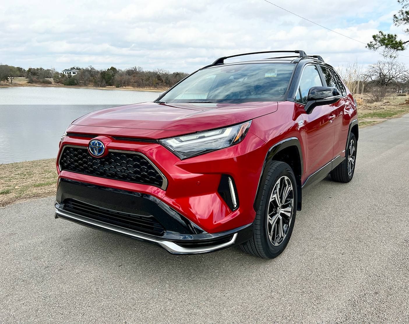 Red SUV parked on a road beside a lake, viewed from the front-left angle.