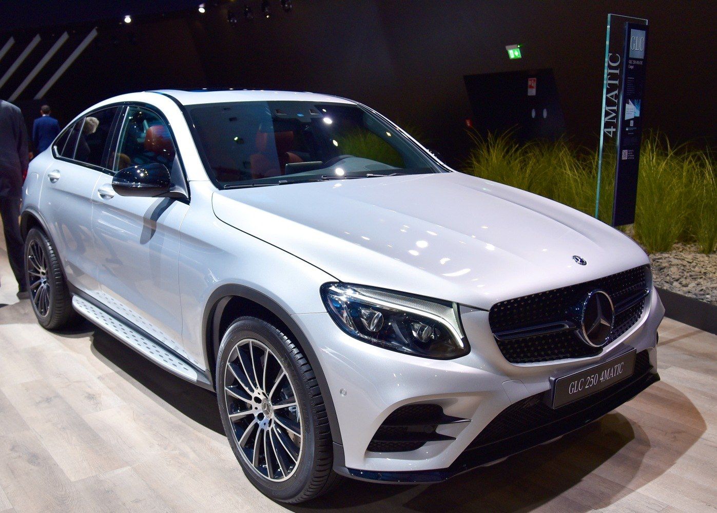 Silver Mercedes SUV on display indoors, angled front view with bright lights.