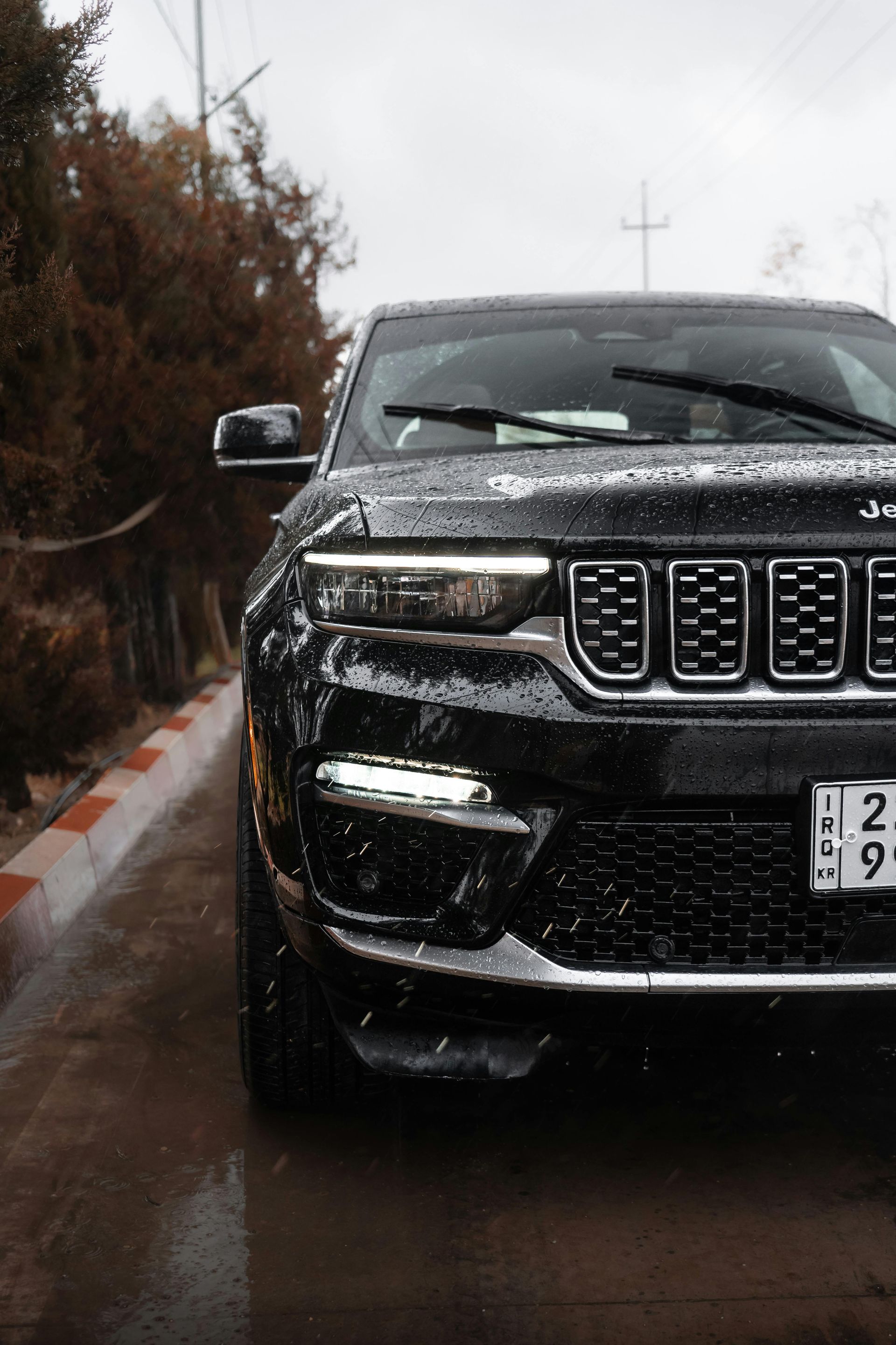 Black SUV on a wet road in the rain, front view with headlights on