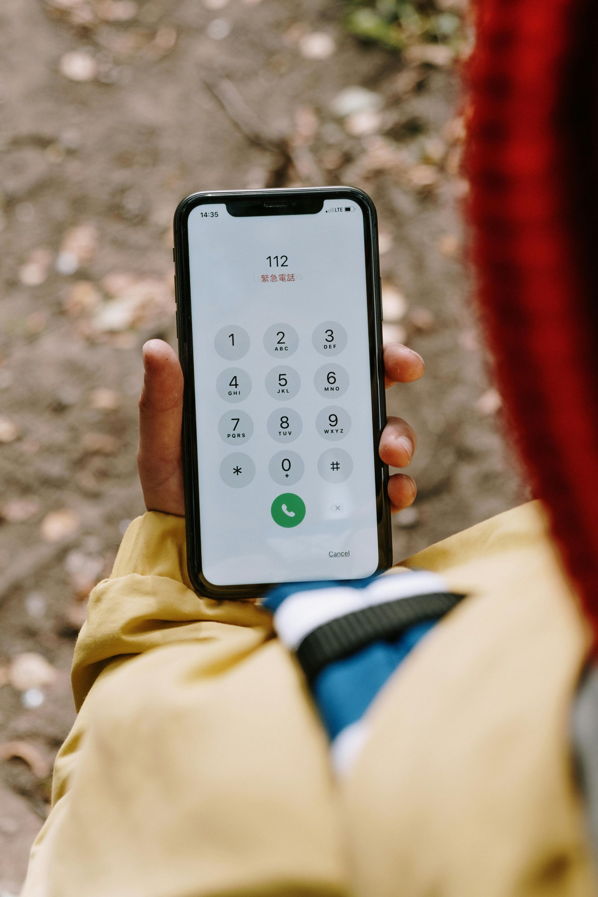 Hand holding a smartphone showing a dial pad outdoors, with a blurred person in the foreground