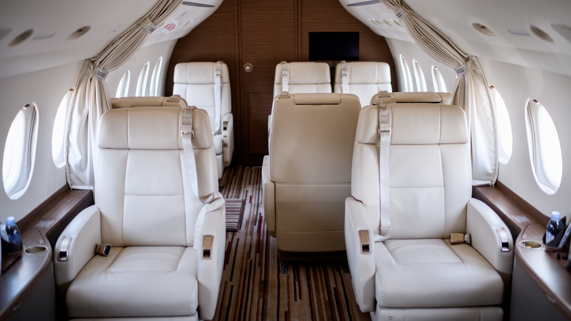 Luxury private jet cabin with white leather seats, oval windows, and wood-paneled walls