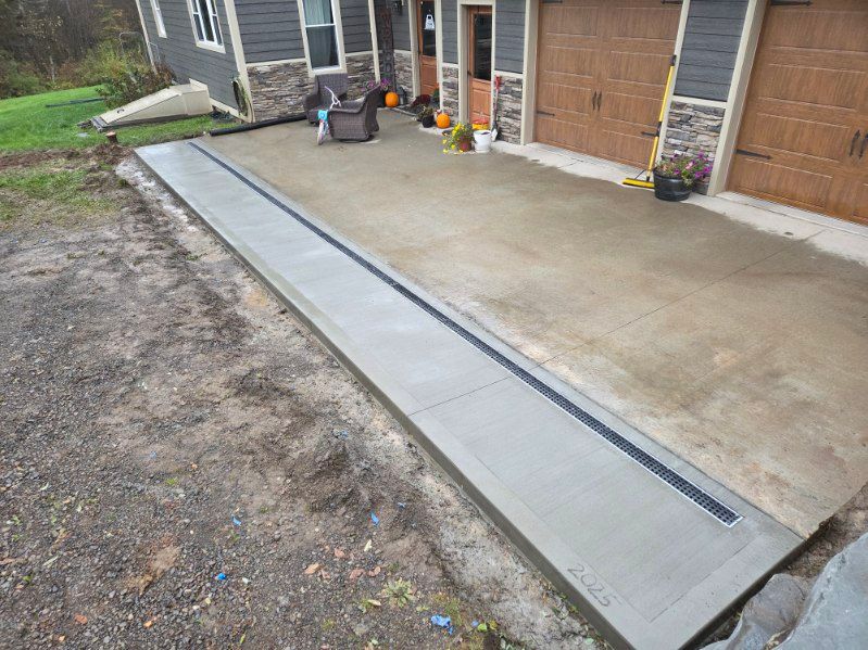 Concrete driveway with a long drain, next to a house and garage.