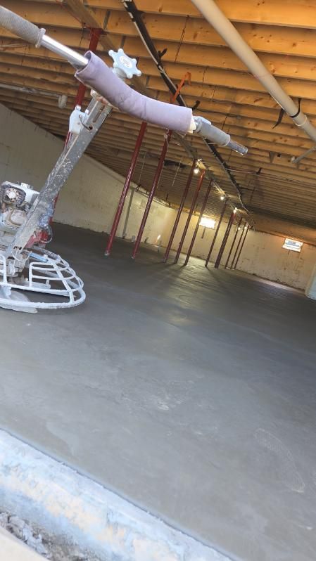 Empty unfinished room with a large robot arm on the left and exposed wooden beams overhead.