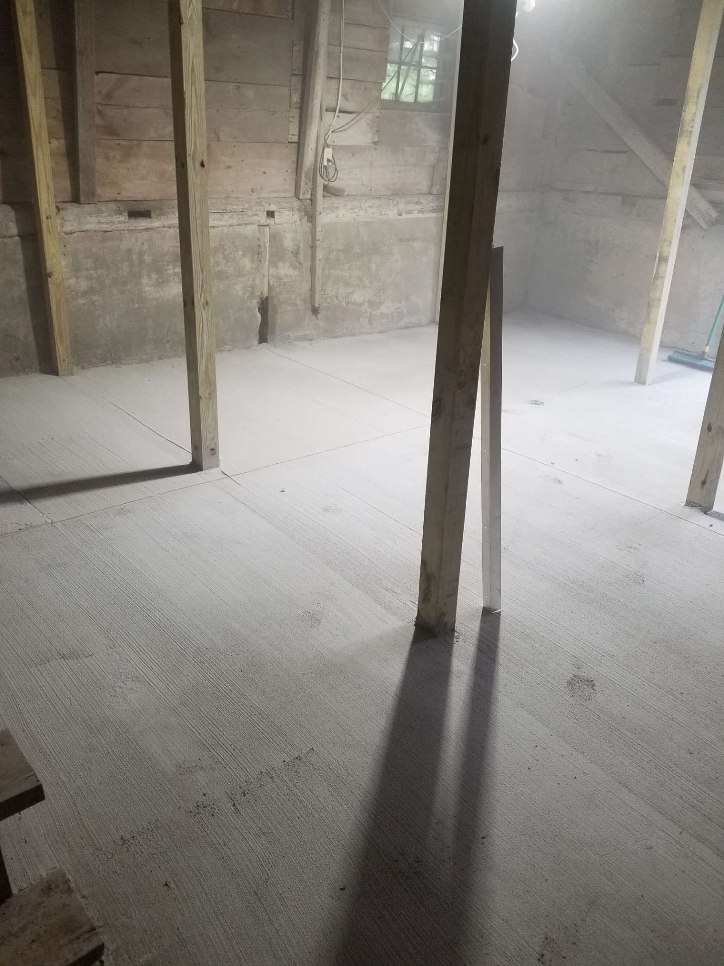 Inside a dusty, unfinished room with wooden supports and a light, concrete floor.