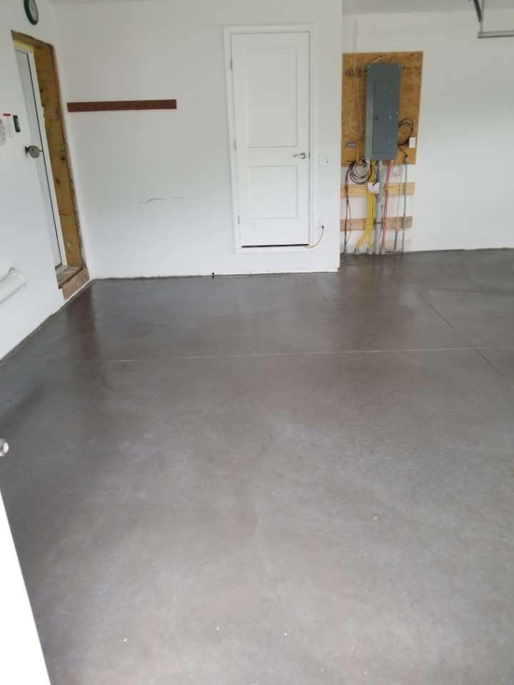Empty garage with gray floor, white walls, and a white door. Electrical panel on the right wall.