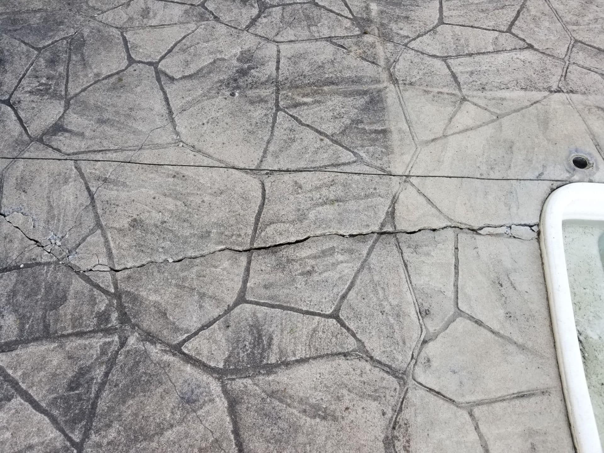 Cracked, patterned concrete paving near a pool. Grey and dark grey stones with black lines.