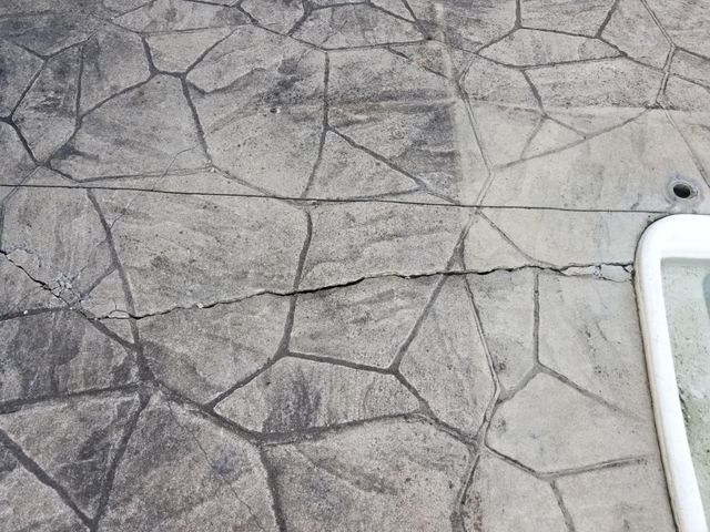 Cracked concrete patio with a flagstone pattern, next to a white pool edge.
