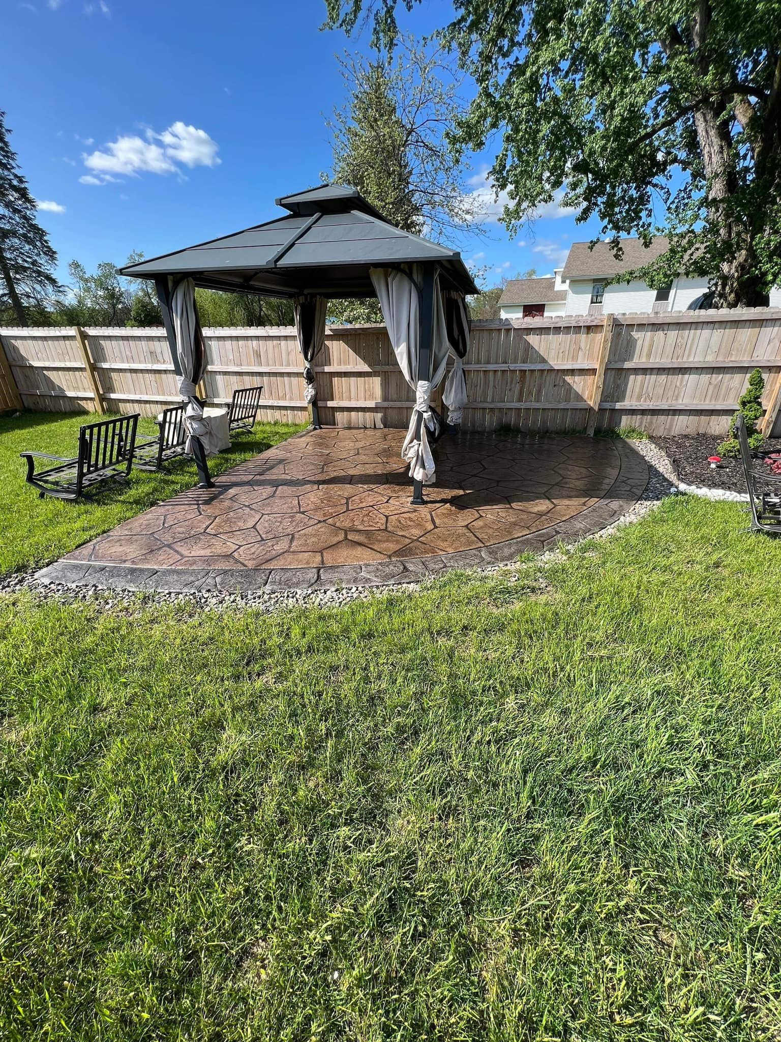 Gazebo on a brick patio in a backyard, with a wooden fence and green grass.