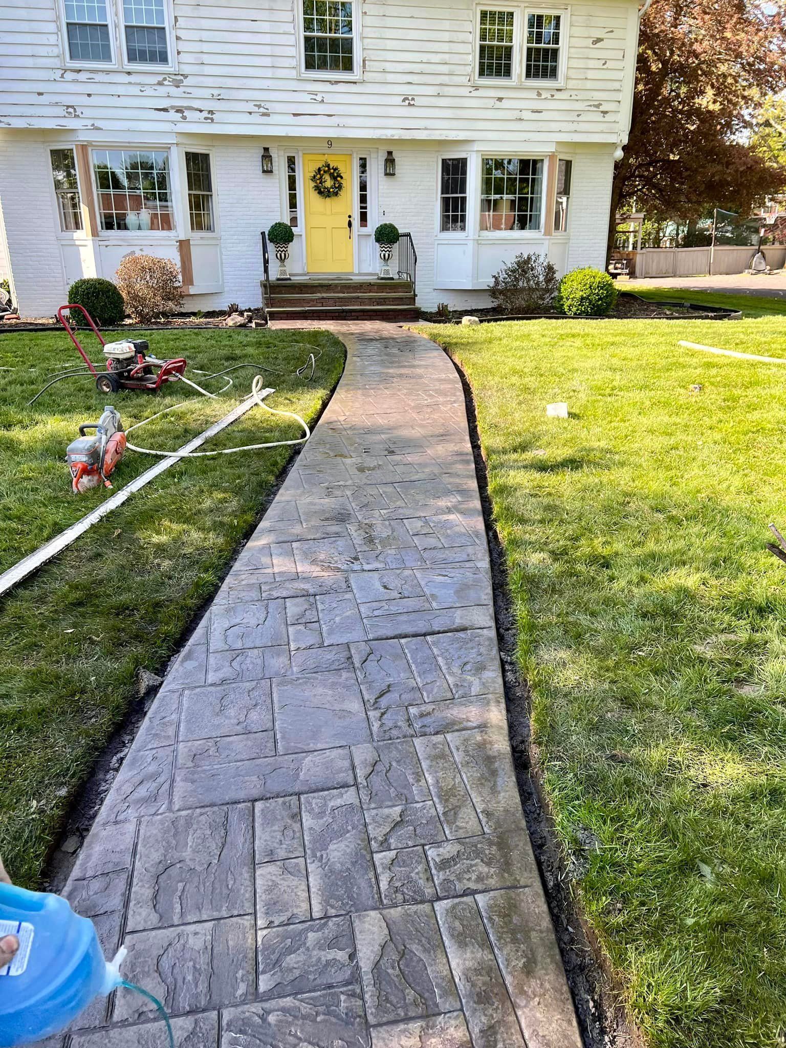 Brick walkway leading to a two-story house with a yellow door, surrounded by green lawn.
