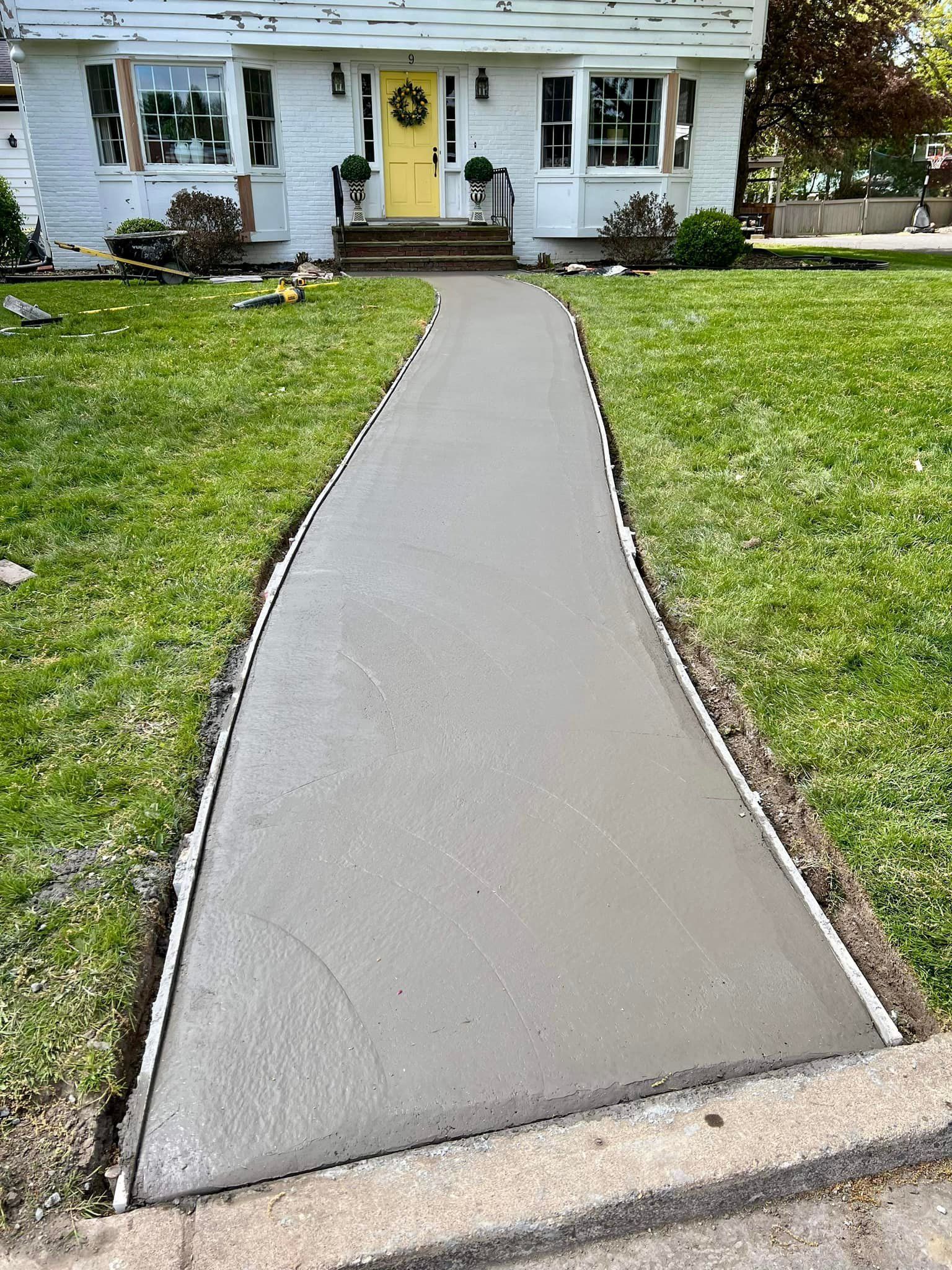 Newly poured concrete walkway leading to a white house with a yellow door.