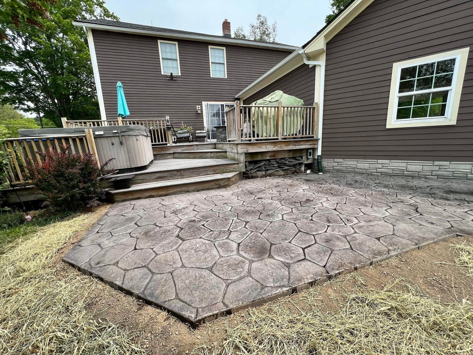 Patio with stamped concrete, wooden deck, and brown house.