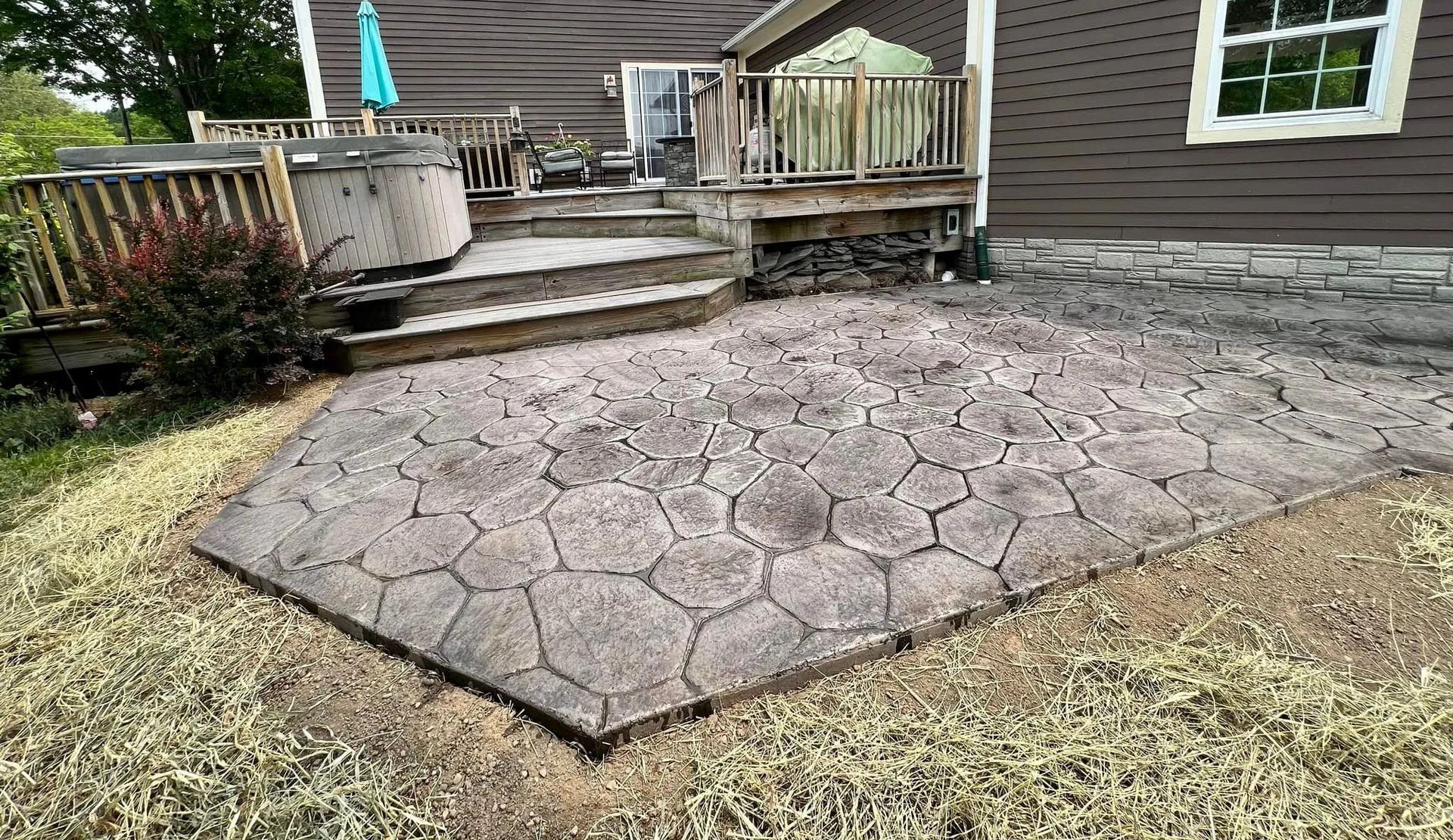 Stamped concrete patio beside a wooden deck and house, with hexagon pattern and steps leading up.