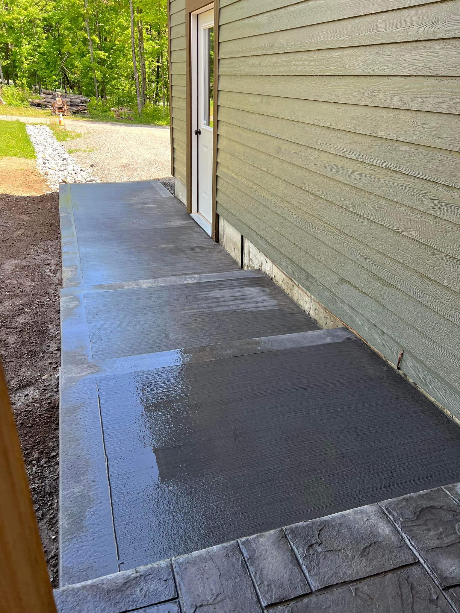 Concrete steps leading to a door next to a green-sided building; a paved walkway.