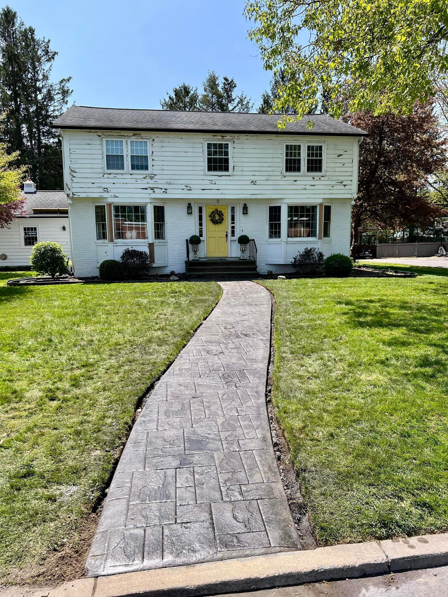 Two-story white house with a yellow door, approached by a brick walkway, set in a grassy yard.