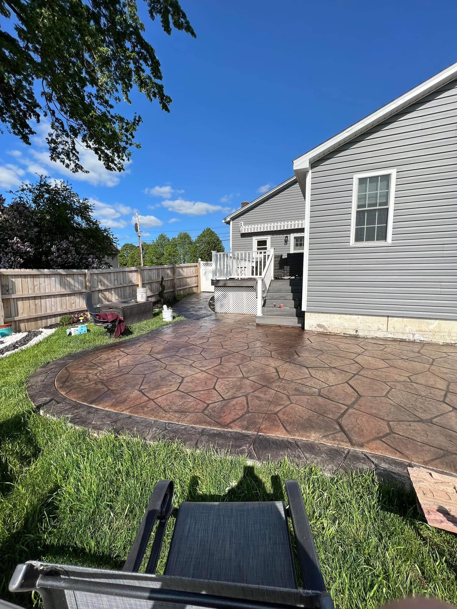 Backyard with a stamped concrete patio, deck, gray house, and a wooden fence on a sunny day.