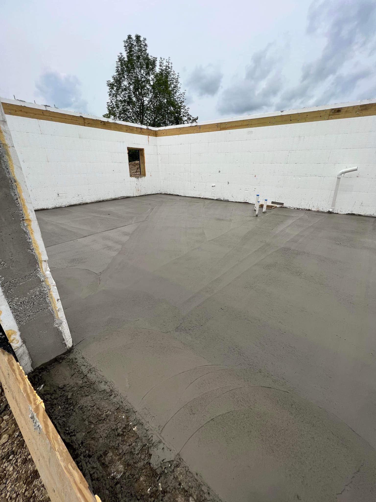 Concrete floor being poured inside a white-walled structure under a cloudy sky.