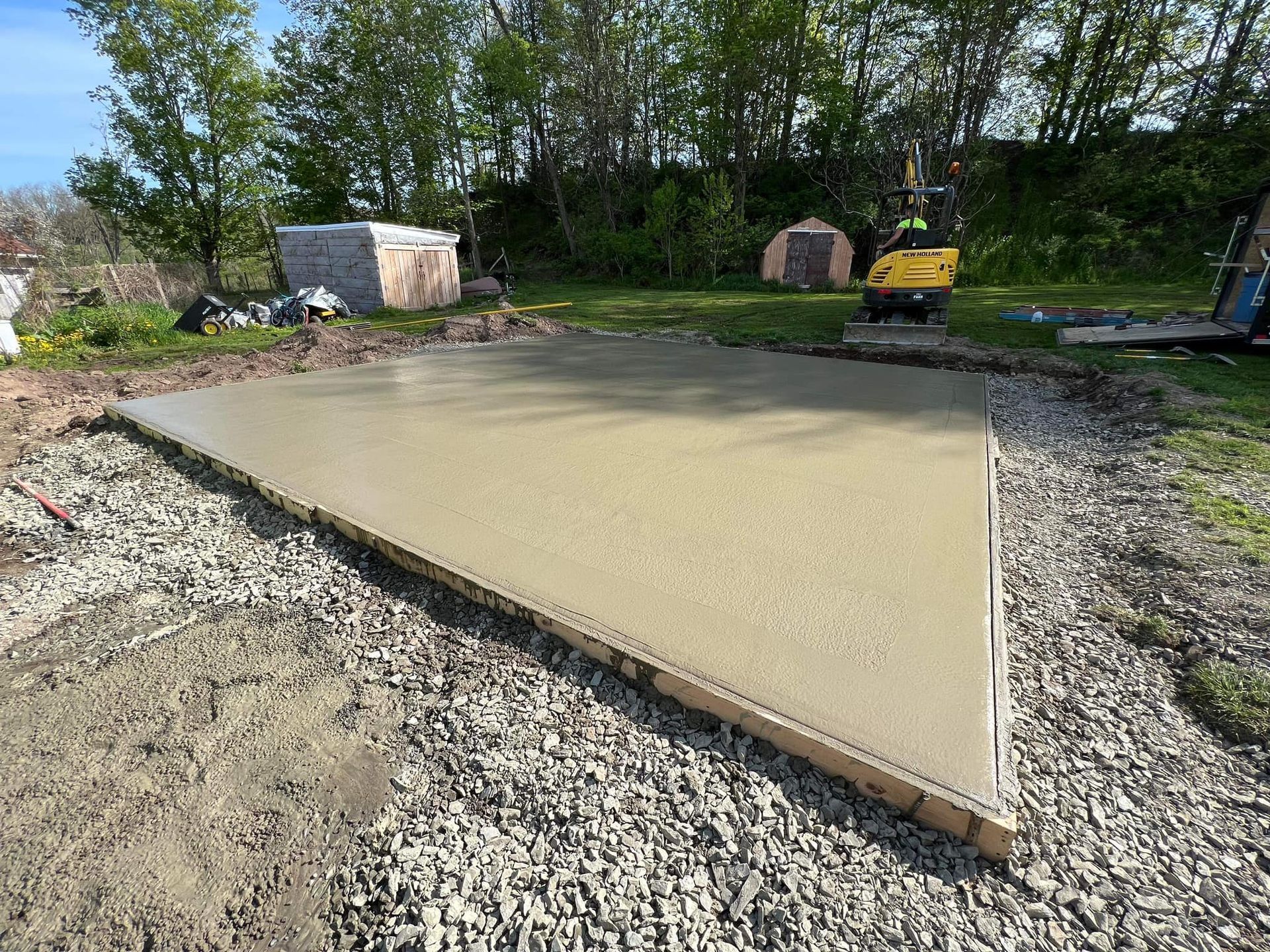 Freshly poured concrete slab in triangular wooden frame, outdoors on gravel.
