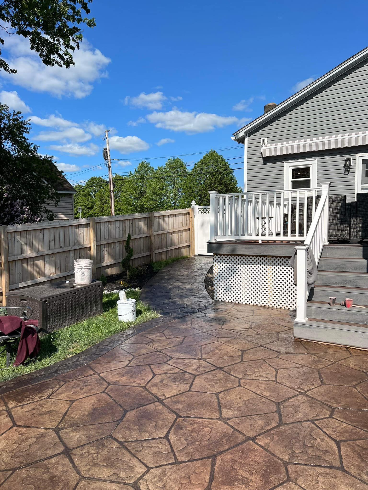 Backyard with stamped concrete patio, deck, fence, and house under a blue sky.