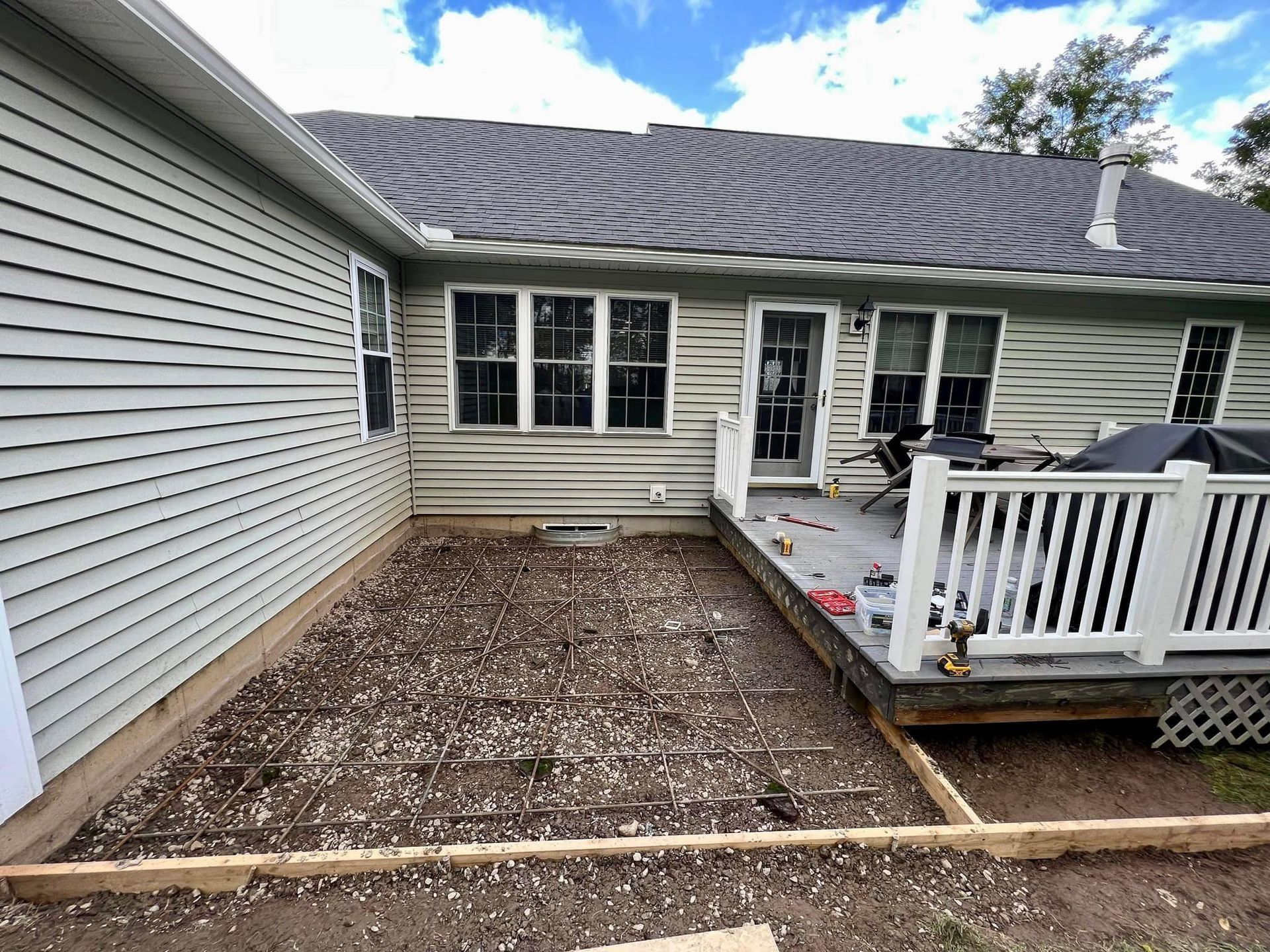 Construction site: prepared ground with rebar next to a wooden deck attached to a light-colored house.