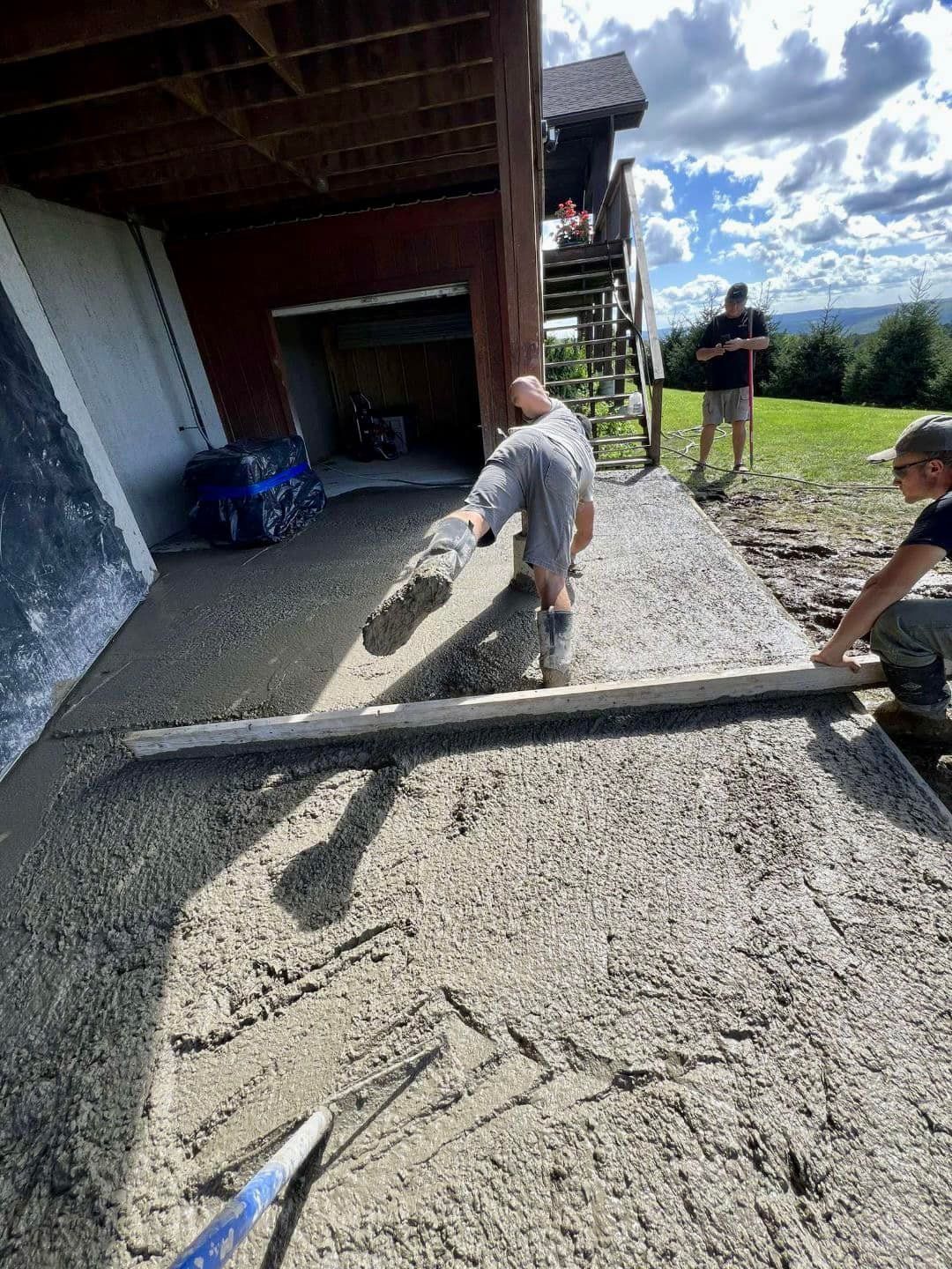 Construction workers leveling wet concrete path next to a building on a sunny day.