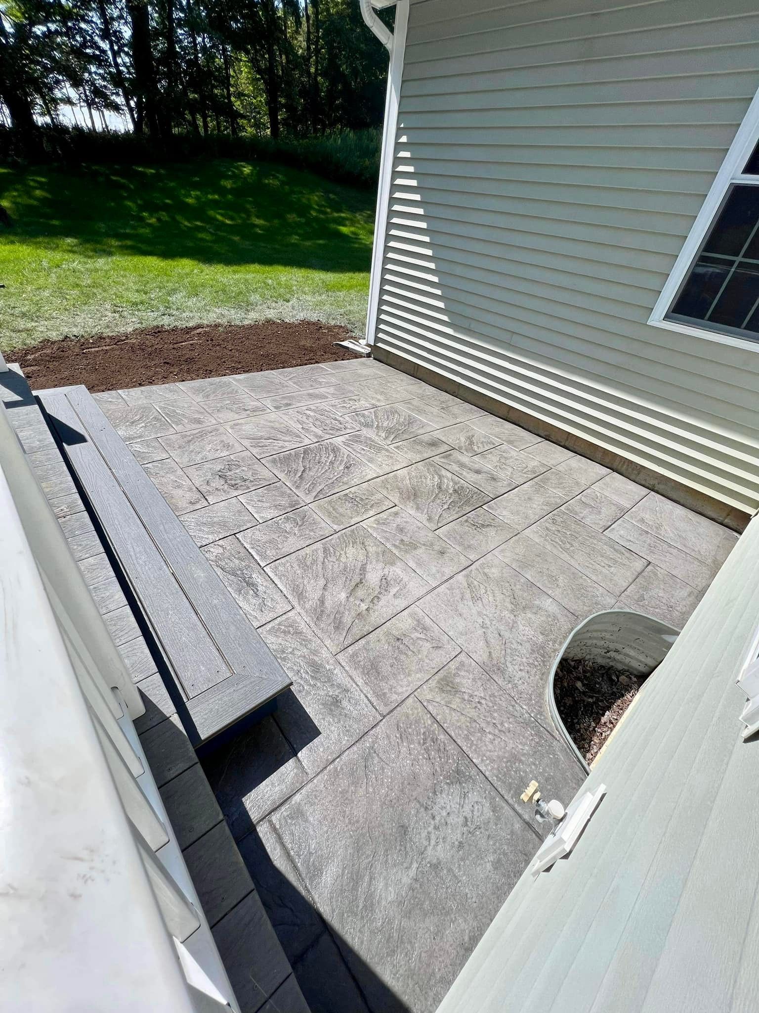 A concrete patio next to a house with a small retaining wall and mulched area.