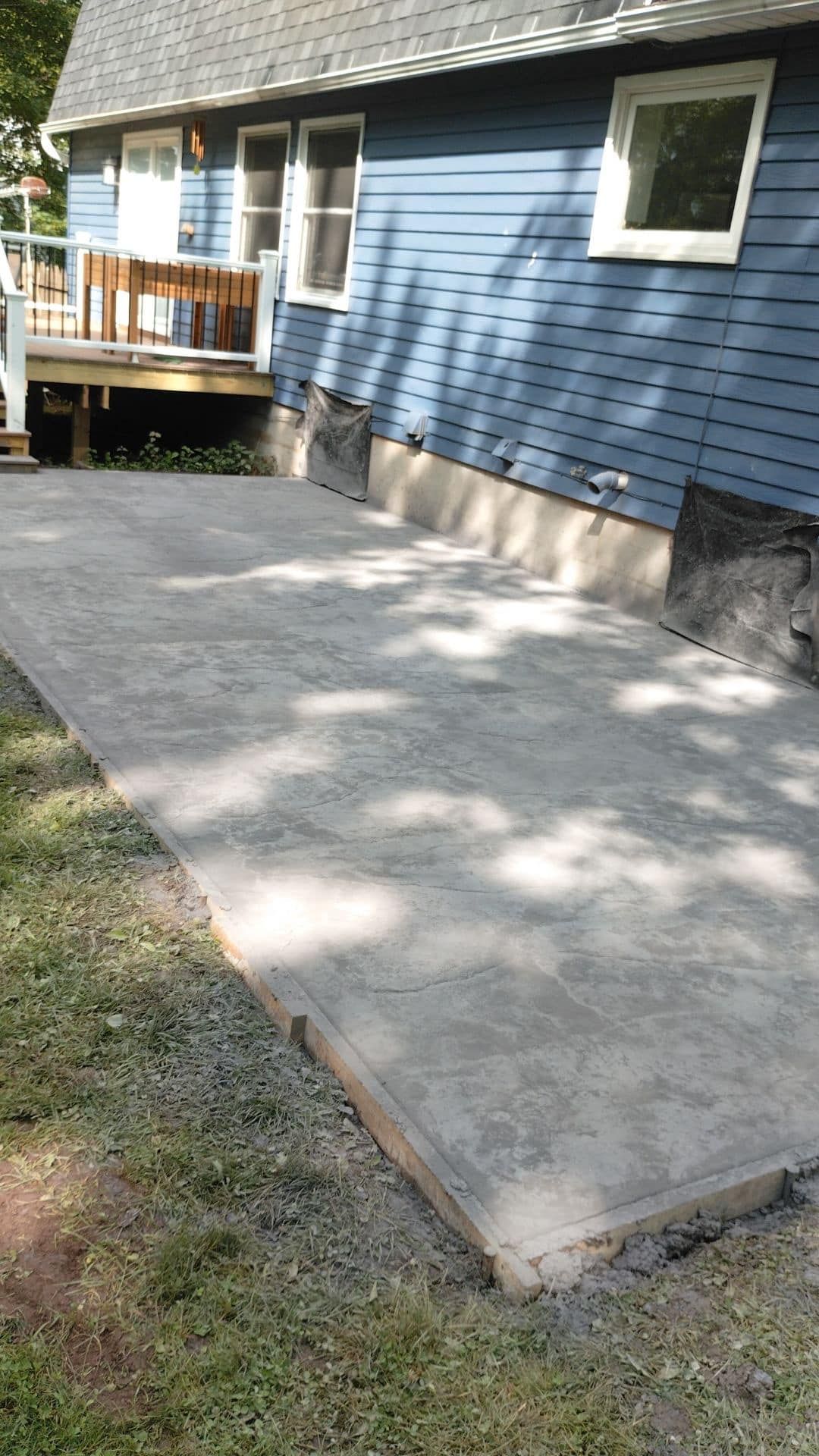 Concrete patio next to a blue house with gravel edging and grass.