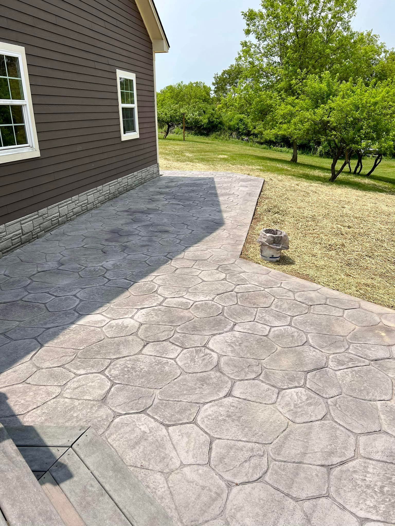 Concrete patio with cobblestone pattern, next to a brown house and gravel.