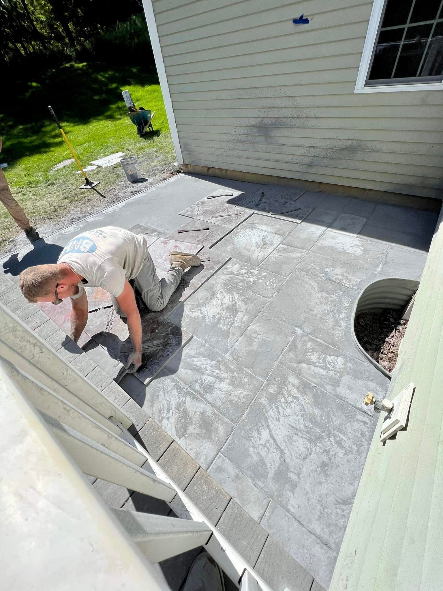 Man installing gray pavers on a patio next to a house.