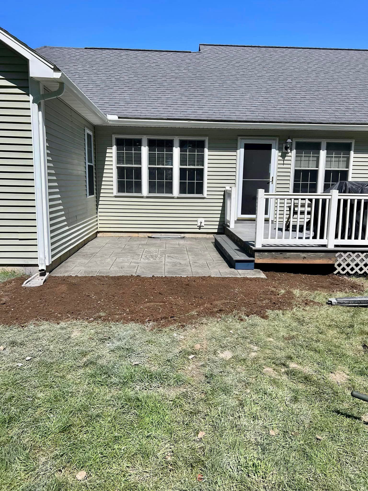 Backyard patio with grass, dirt, and a deck attached to a house.