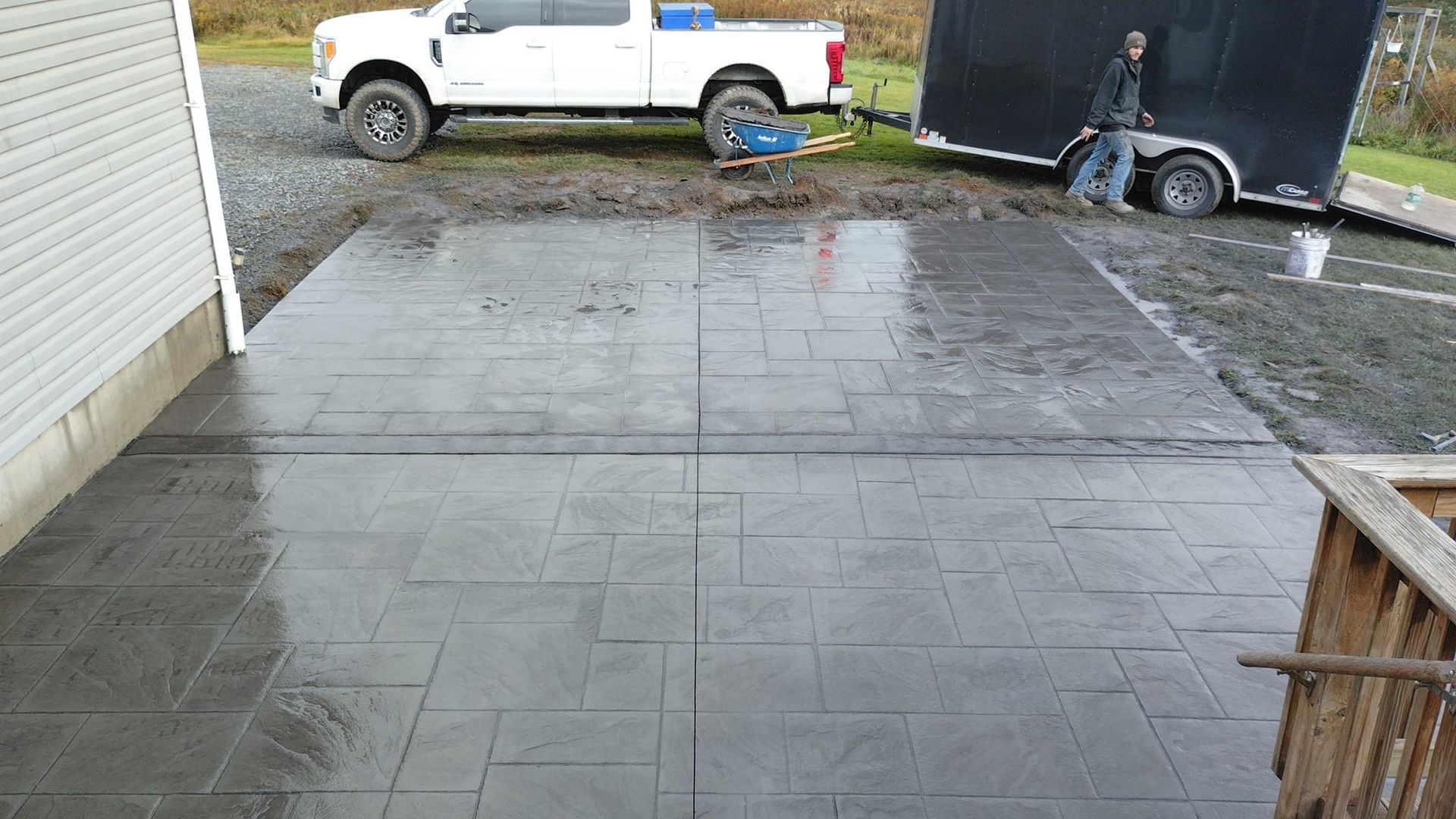 A freshly poured concrete patio in front of a white truck and trailer; a person stands nearby.