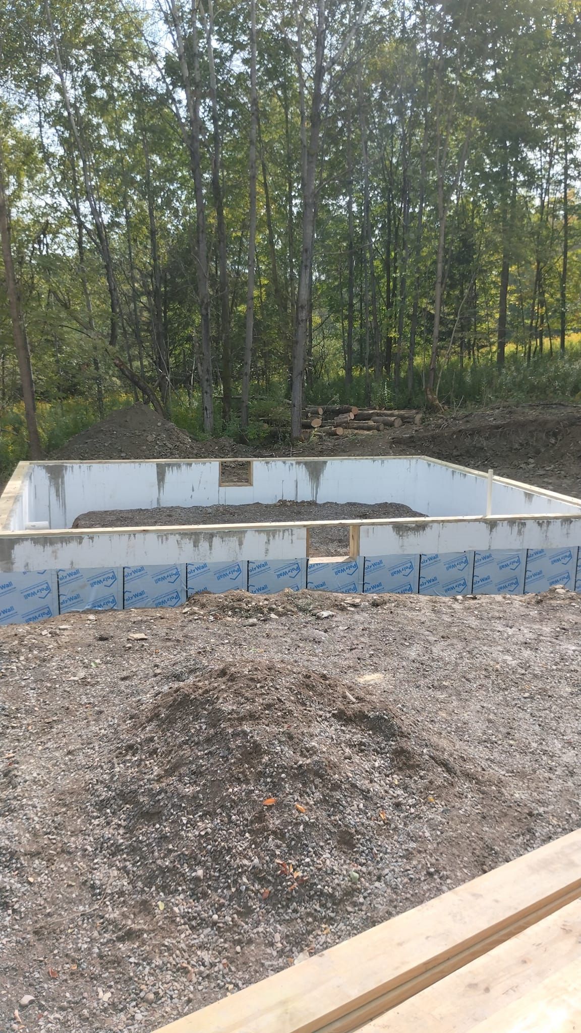 Foundation of a building with gravel in front, trees in the background.