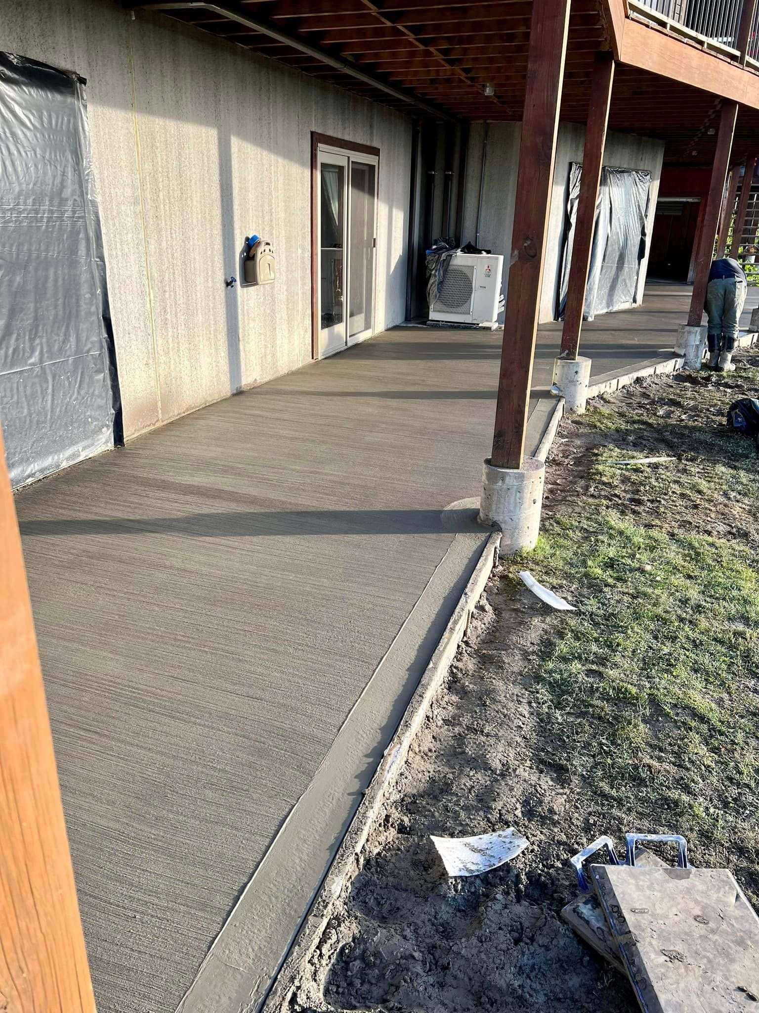 Concrete walkway with a covered porch. A door and grassy area are visible.