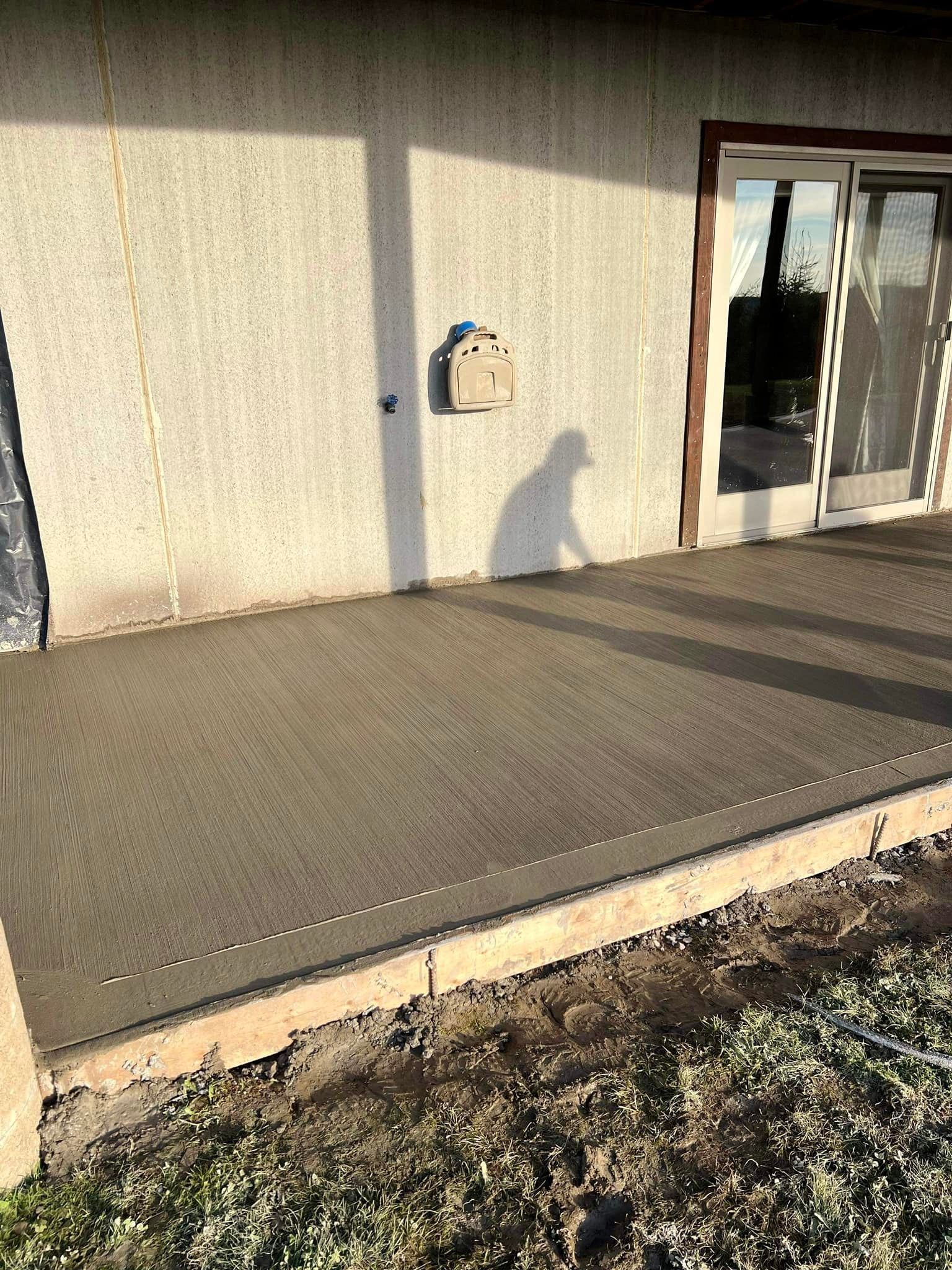 Freshly poured concrete patio against a stucco wall, next to a sliding glass door.