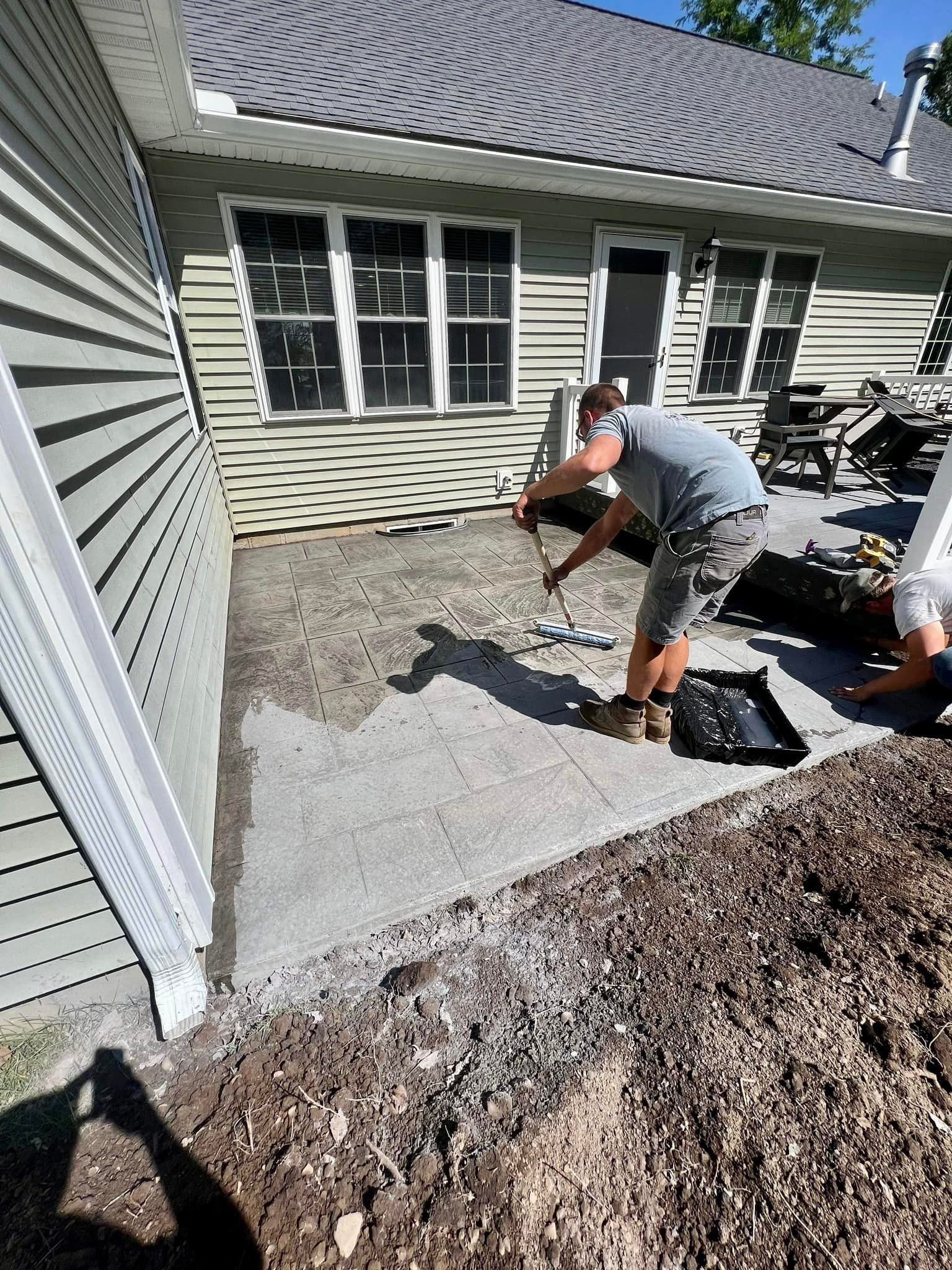 Person smoothing concrete on a patio beside a house.