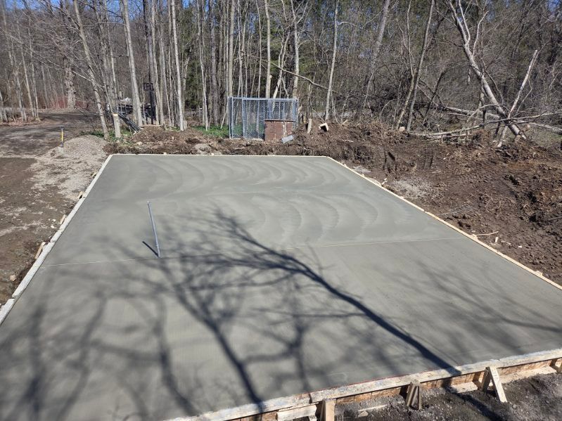 Freshly poured concrete slab with a small pipe in a wooded outdoor area