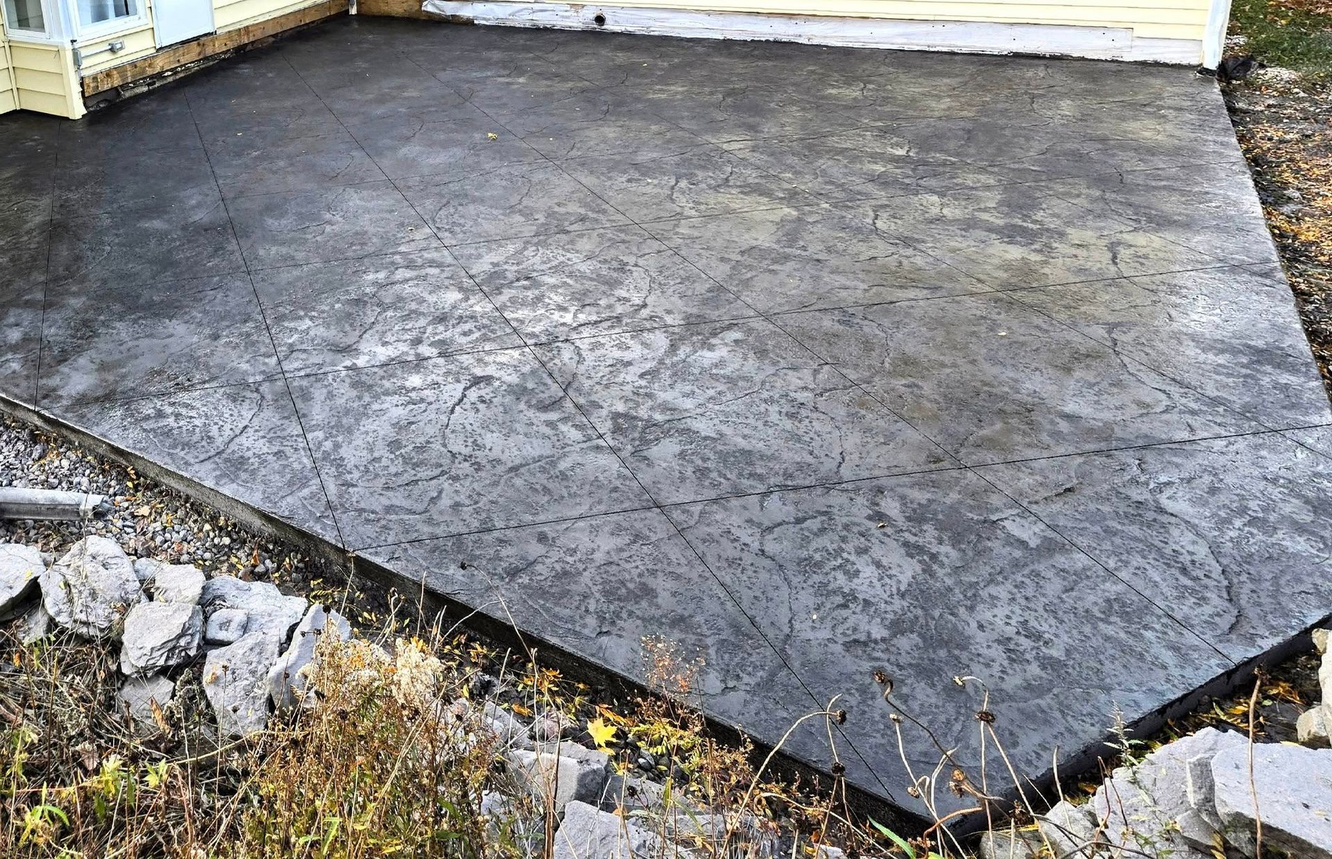 Concrete patio with textured surface, dark gray color, adjacent to a building.