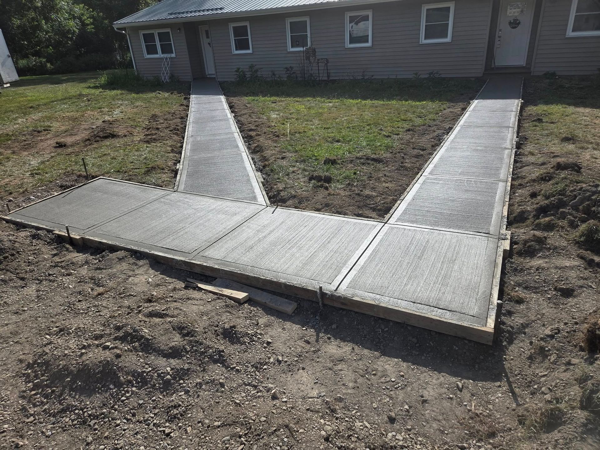 Newly poured concrete sidewalks leading from a building with grass and dirt ground.