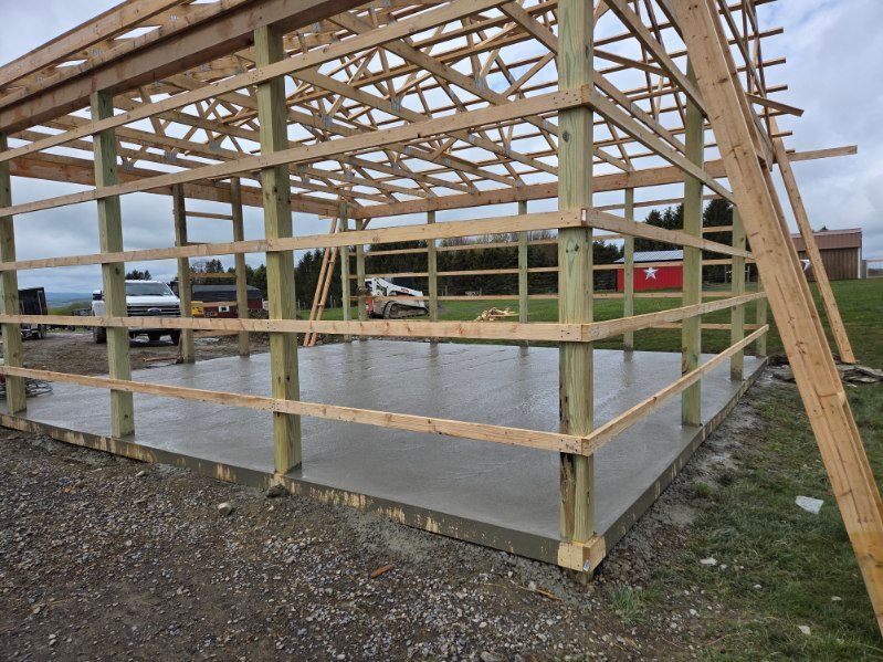 Wooden post-and-beam barn frame under construction on a concrete slab outdoors
