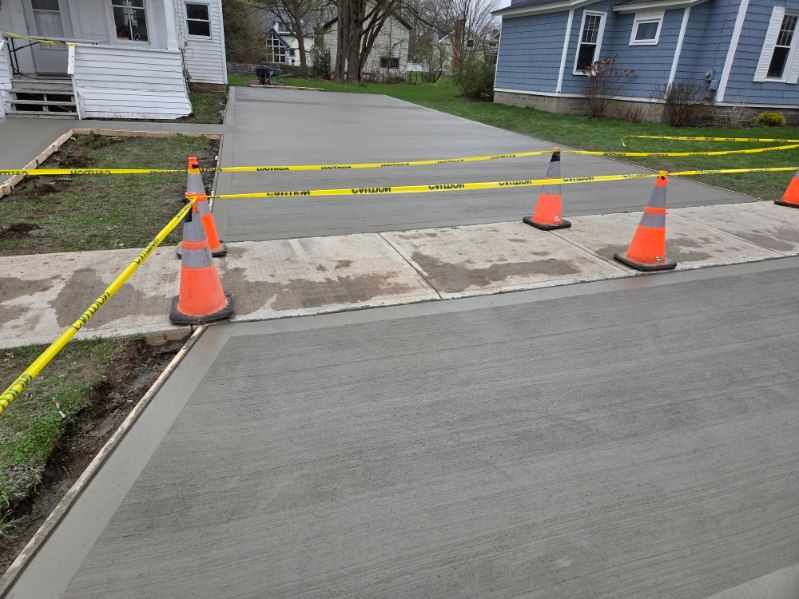 Blocked residential driveway with orange cones and caution tape near a sidewalk and curb cut
