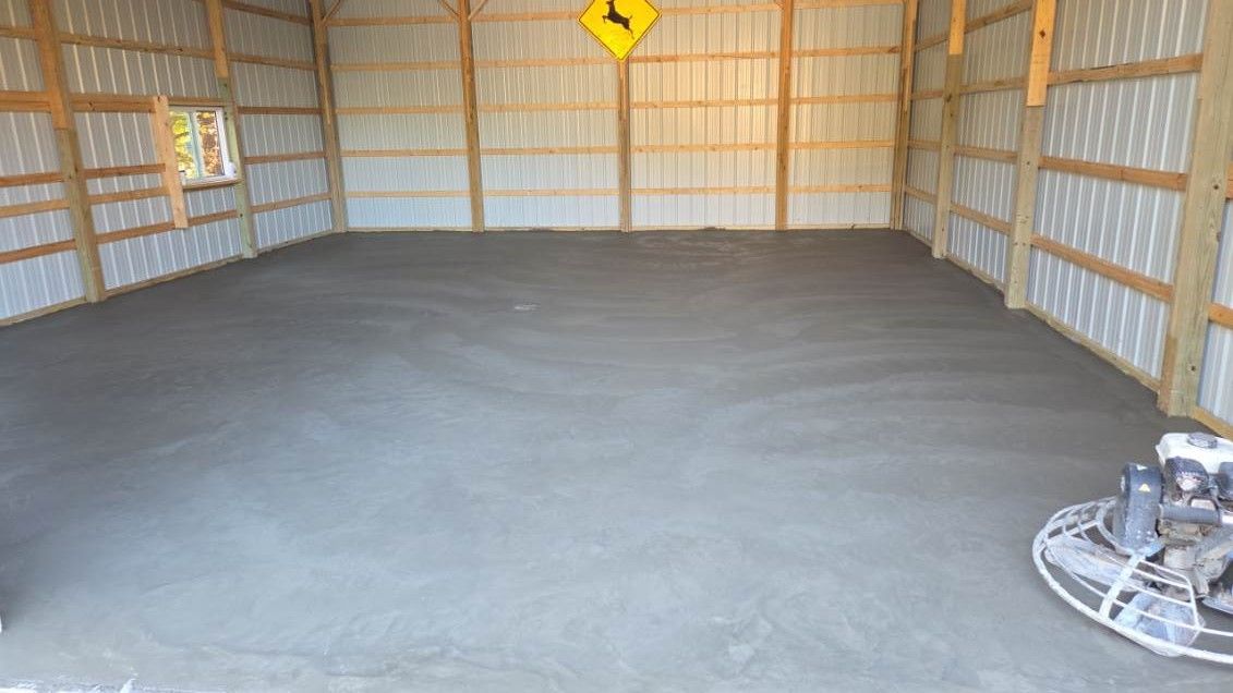 Newly poured concrete floor inside a wooden-framed barn with metal siding.