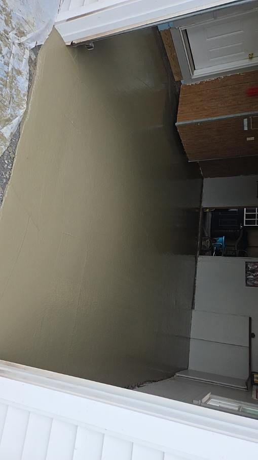 Empty covered patio with beige floor, white trim, and brick wall beside a white fence and windows