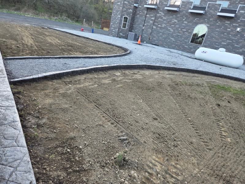 Stone walkway beside a freshly graded dirt yard with a stone retaining wall and two orange cones in the background