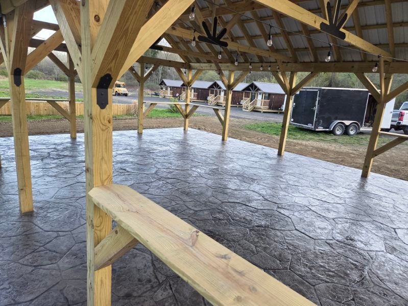 Wooden pavilion with a wet concrete floor and black trailer in the background on a rainy day