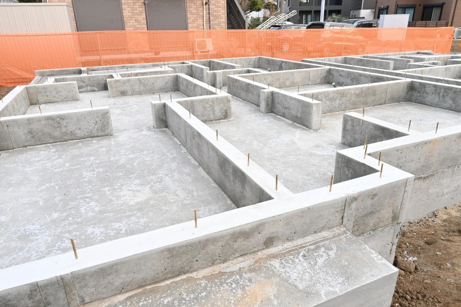 Concrete foundation of a building under construction, with forms for walls. Orange construction fencing.
