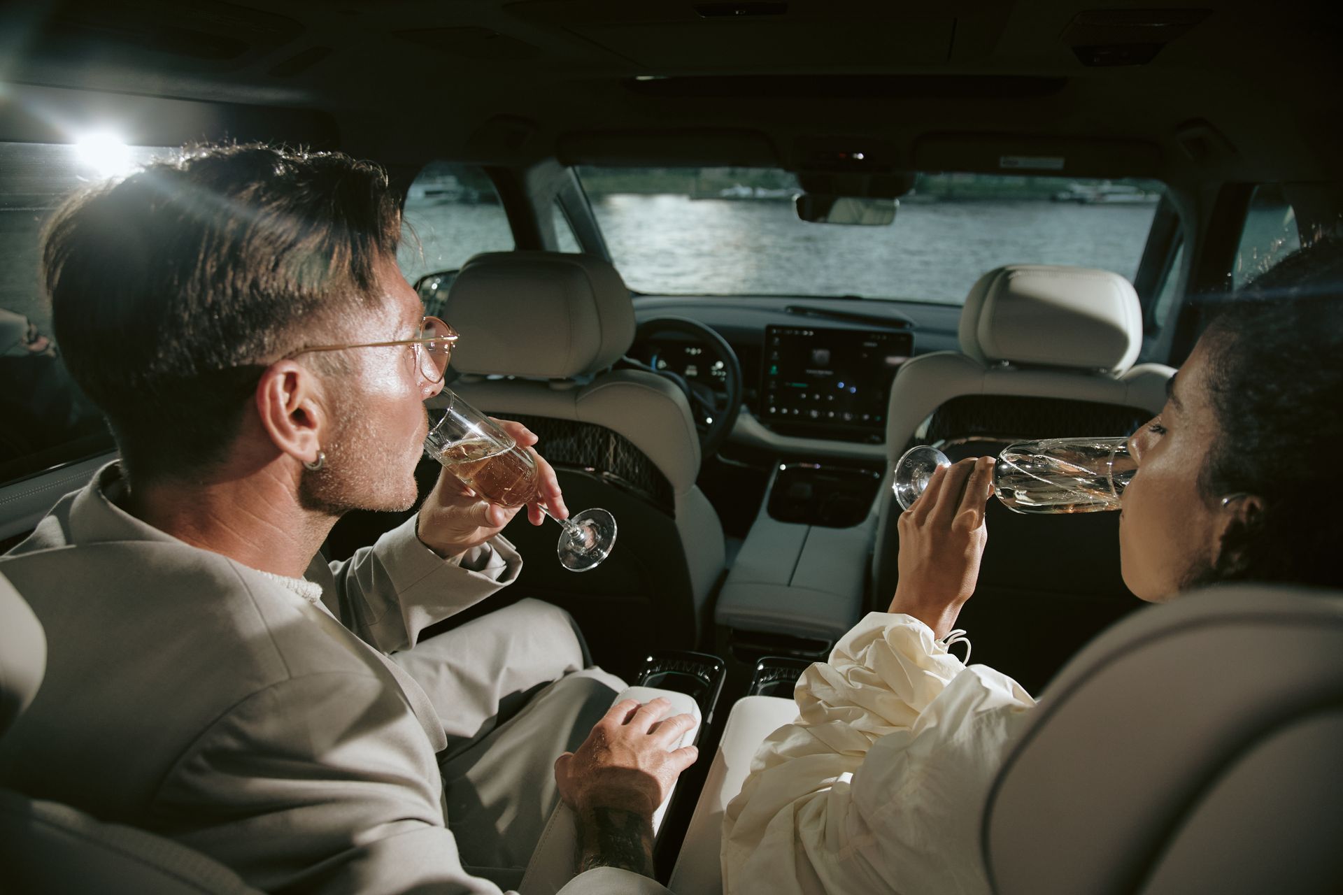 Two people in a car sharing drinks, seen from the back seat at night.