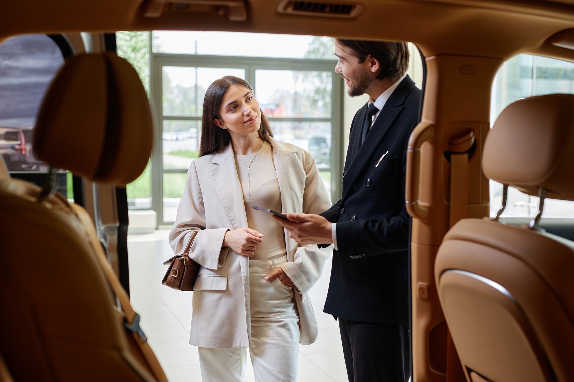 Two people chatting beside a car, with brown leather seats visible in the foreground.