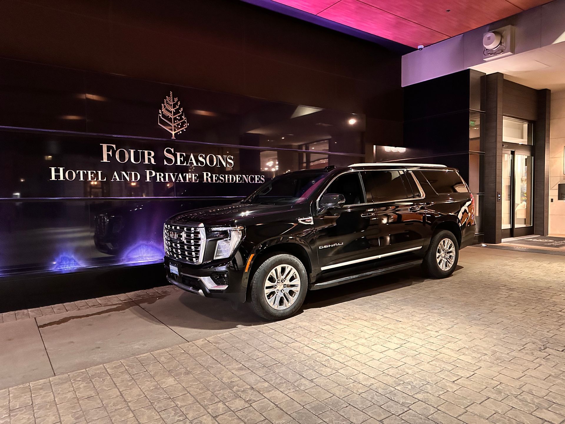 Black SUV parked at the Four Seasons Hotel entrance with logo in dark background.