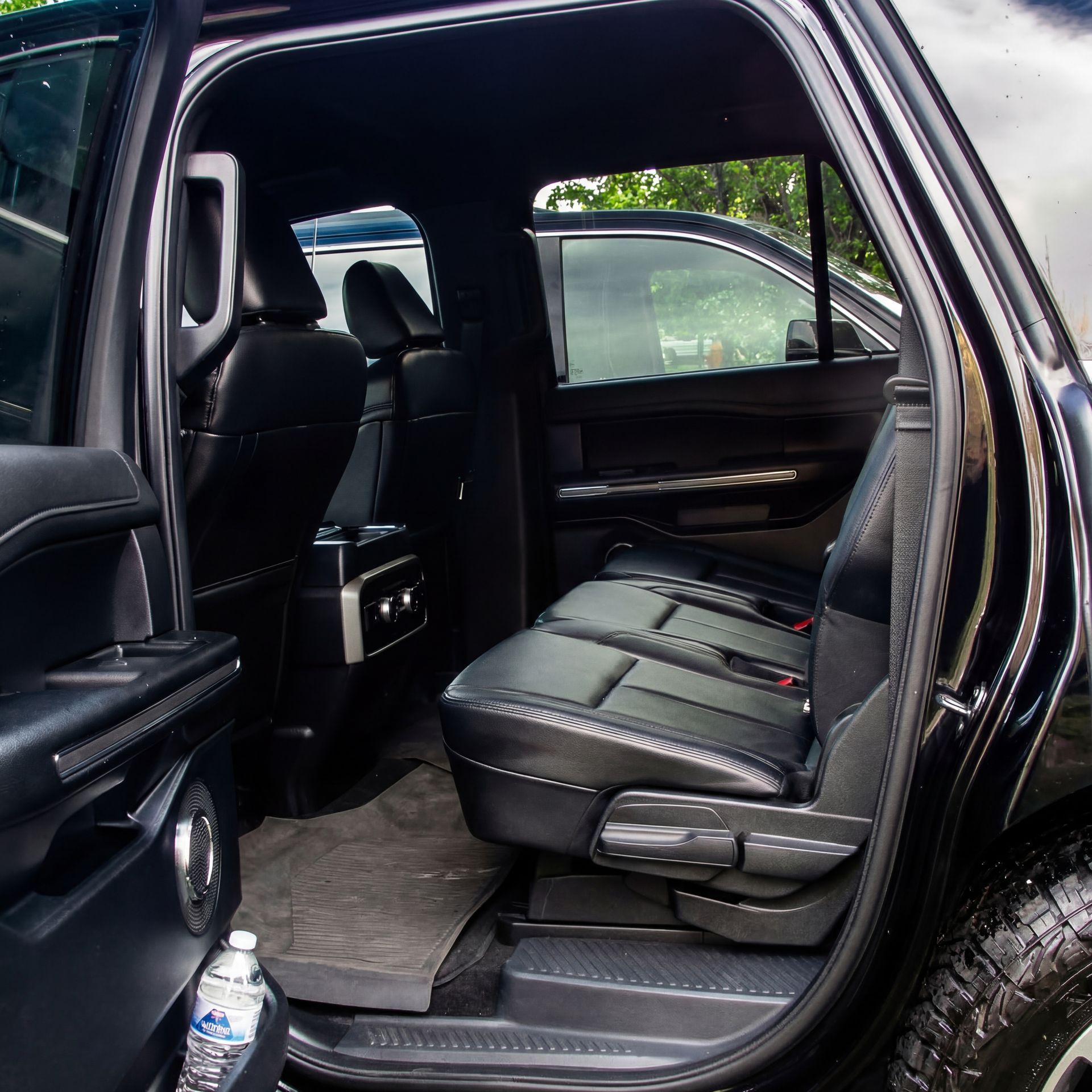 Black SUV interior with open door, showing rear seats, center console, and water bottle.