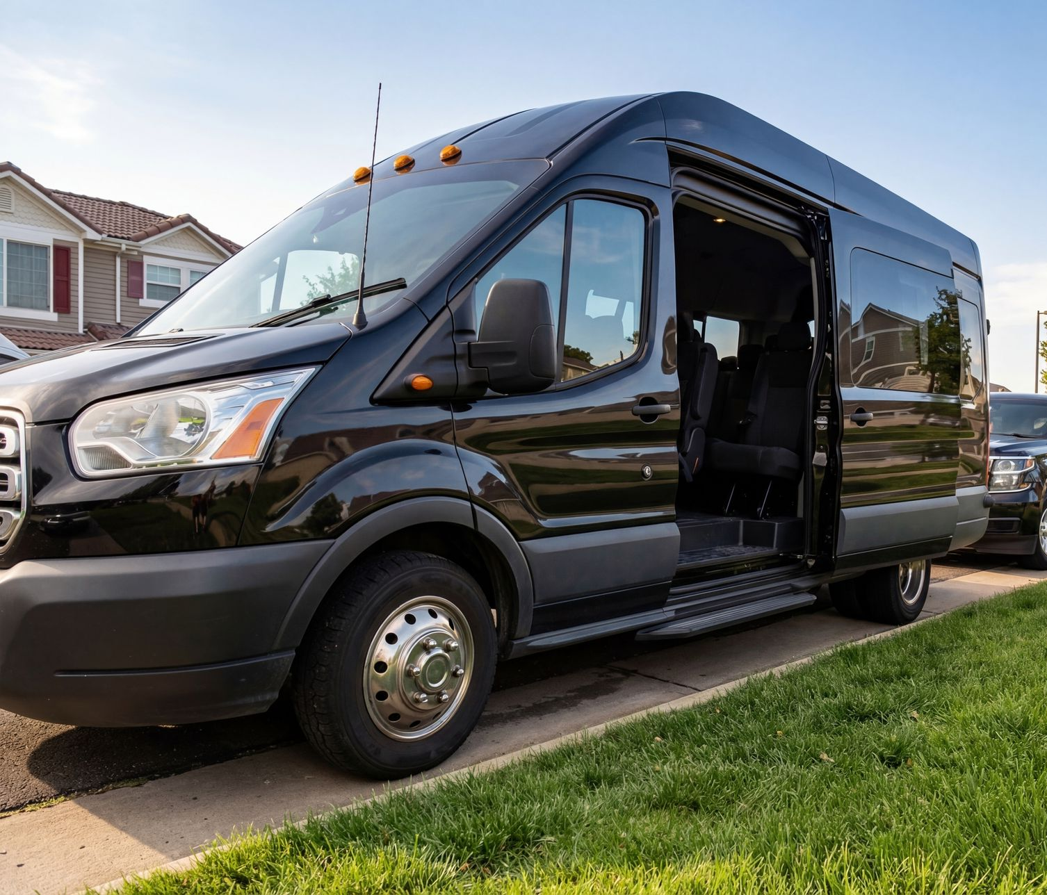 Black passenger van with sliding door open parked on a curb in front of a house.